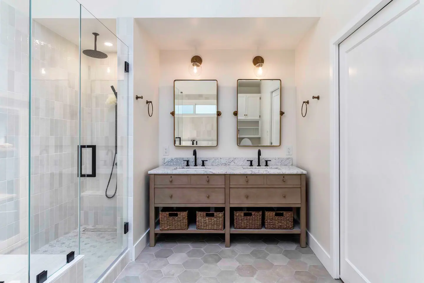 Double vanity in natural wood with wicker baskets, brass sconces and a glass shower